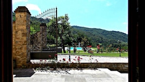A stone entrance gate leading to a courtyard with a pool, surrounded by greenery and hills.