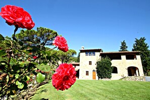Un edificio in pietra con tetto in tegole, un prato curato e fiori rossi in primo piano.