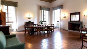 Una habitación amplia con una mesa y sillas de madera, una chimenea y ventanas grandes con cortinas.