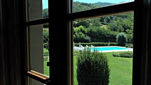 Une vue à travers une fenêtre sur une piscine entourée d’une végétation luxuriante et de collines.