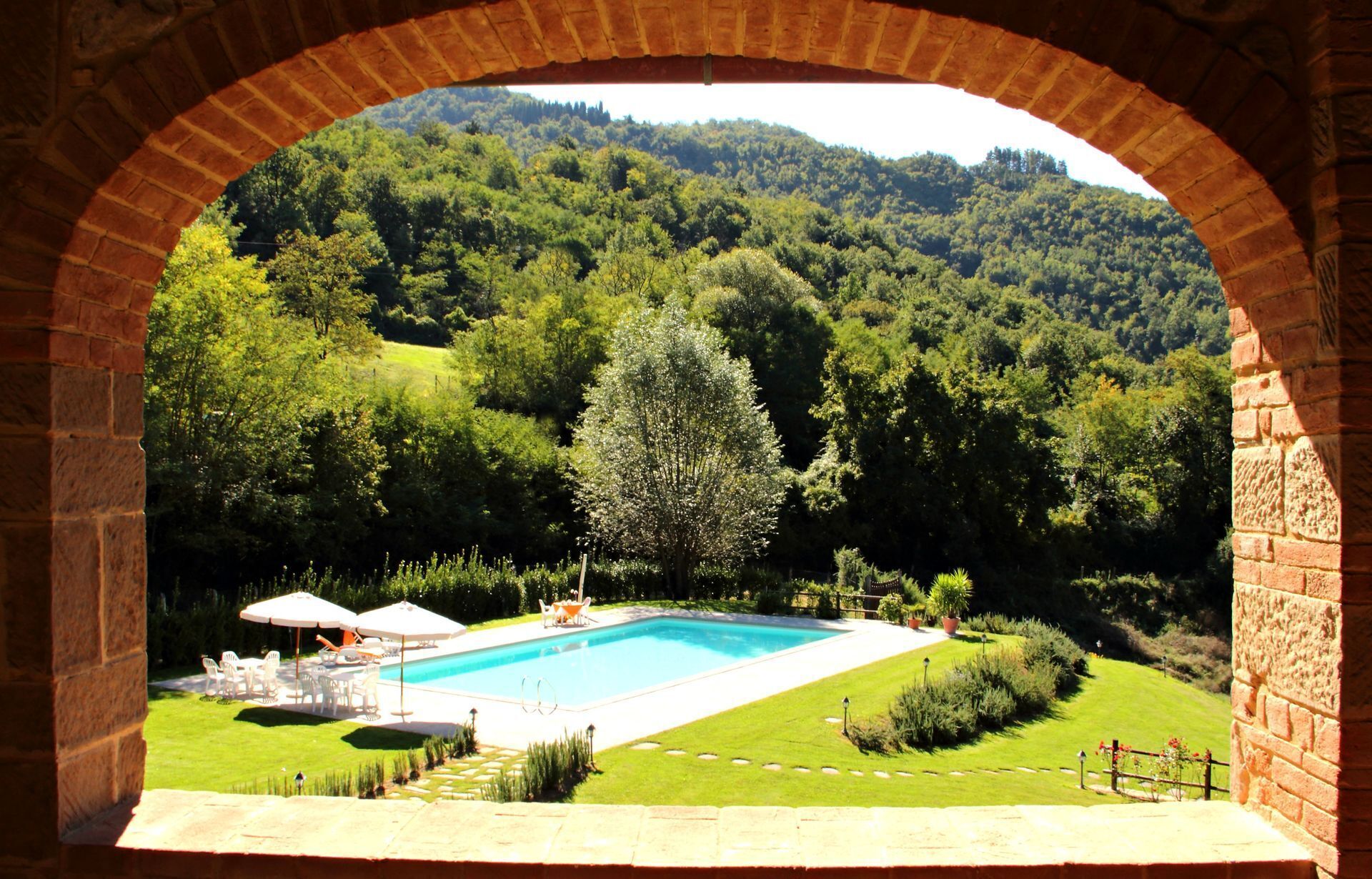 A swimming pool with a patio area, surrounded by lush greenery and a hilly landscape.