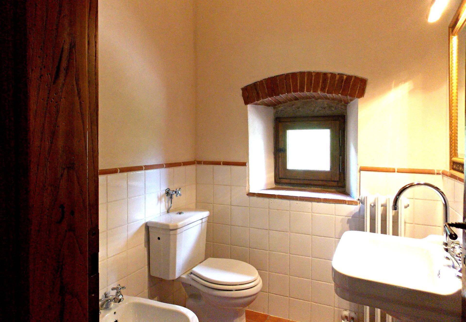 Une salle de bain avec des toilettes, un lavabo et une fenêtre.