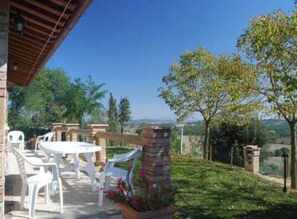 An outdoor patio area with a round table and chairs, surrounded by greenery and a clear view of the landscape.
