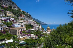 Une ville côtière avec des bâtiments construits sur une colline, une église surmontée d’un dôme doré, et la mer en arrière-plan.