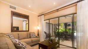 A living room with a sofa, a coffee table, a mirror, and a sliding glass door leading to an outdoor area with furniture. - Sunrise 33- 3 Bedroom Poolside Condo (Tamarindo)