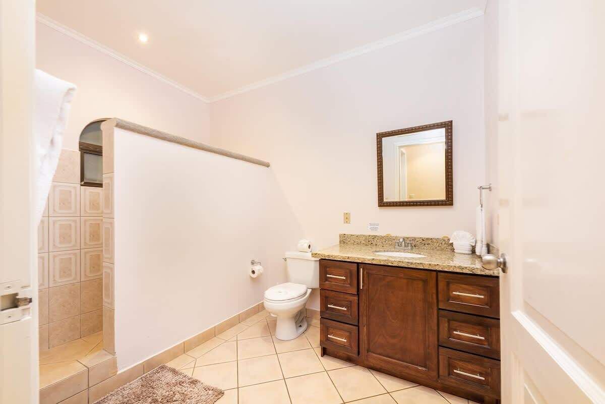A bathroom with a toilet, a sink with a mirror above it, and wooden cabinets.