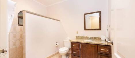A bathroom with a toilet, a sink with a mirror above it, and wooden cabinets.