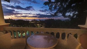 Un balcon doté de meubles en osier et offrant une vue sur un coucher de soleil se déclinant sur un paysage.