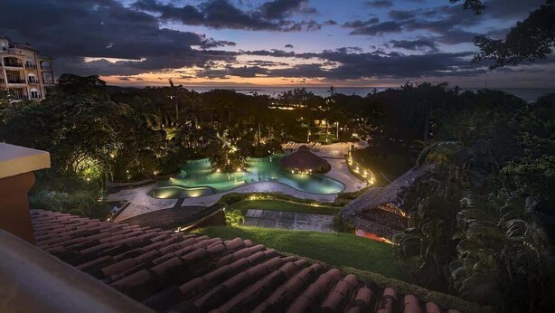Un complexe hôtelier doté d’une piscine, d’une végétation luxuriante et offrant une vue sur l’océan au crépuscule.