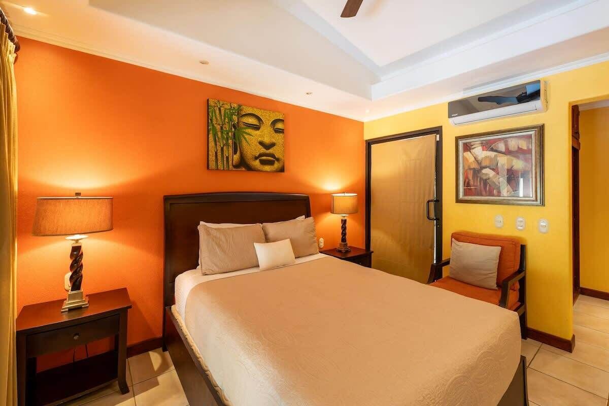 Une chambre d’hôtel avec un grand lit, deux tables de chevet avec des lampes, un climatiseur fixé au mur et une porte.