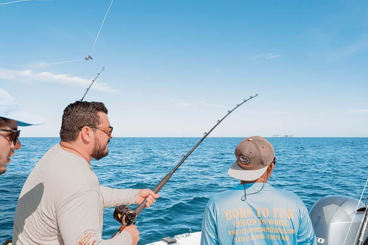 A boat with two individuals fishing, one wearing a cap and a t-shirt with text, and another holding a fishing rod.