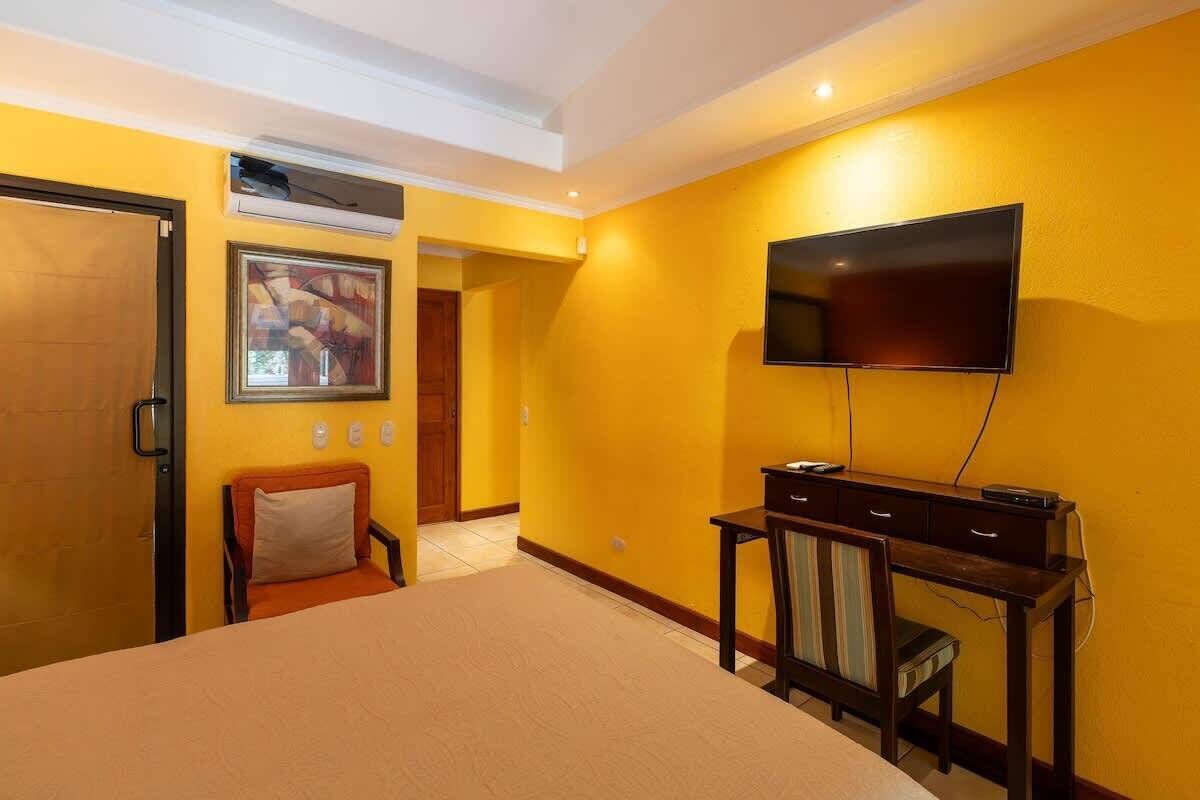Een hotelkamer met een bed, bureau, stoel, televisie en een airconditioning.