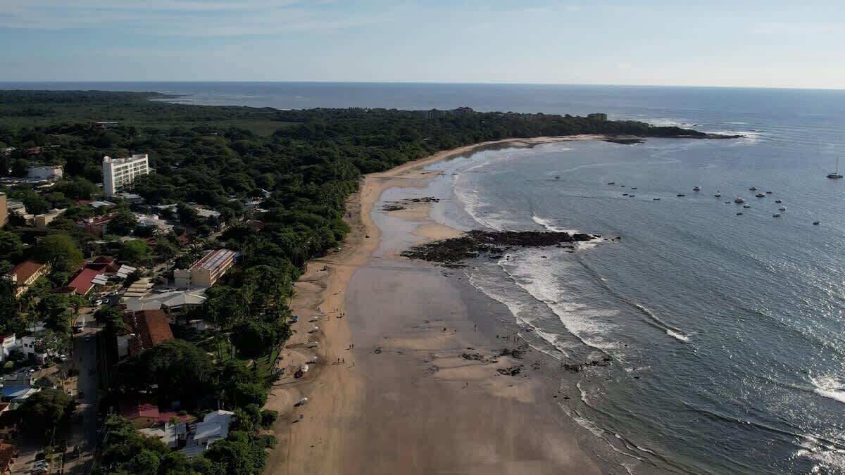 An aerial view of a coastal area with a beach, buildings, and boats.