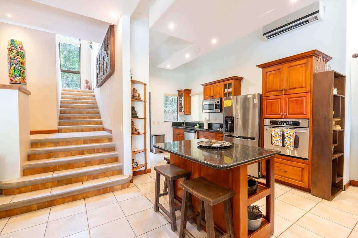 Una cocina con armarios de madera, un refrigerador de acero inoxidable y una isla central con taburetes.