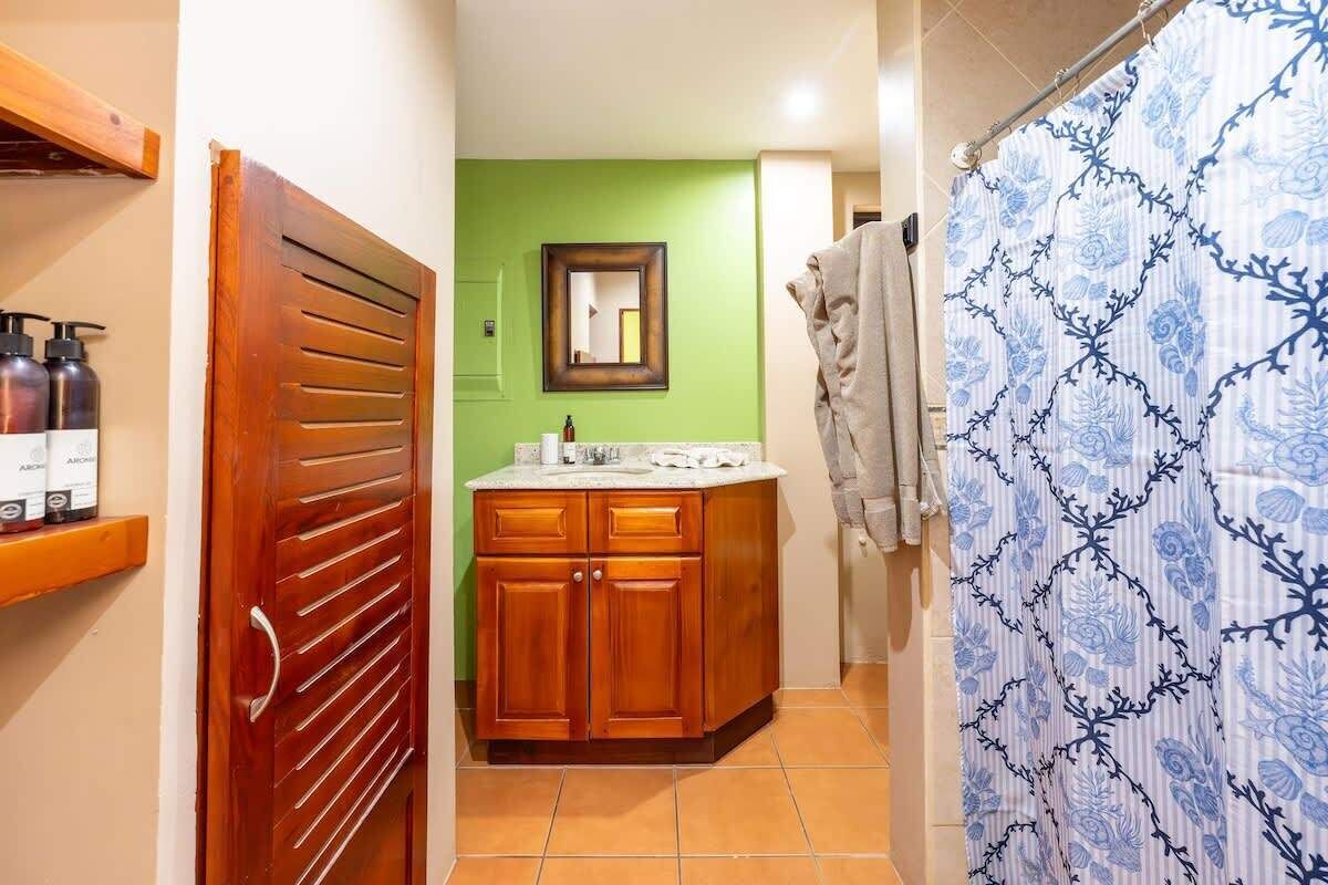 Un baño con tocador de madera, pared verde y cortina de ducha estampada con motivos florales.