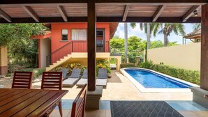 A covered outdoor area with a pool, lounge chairs, and a wooden table. - Jade Coast #3- Private 5 Bedroom Villa (Tamarindo)