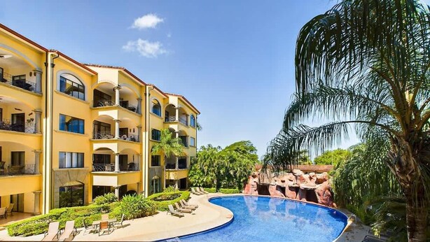 Ein Hotel mit Swimmingpool, Liegestühlen und einer Palme.