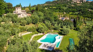A pool surrounded by lush greenery, a stone building, and a distant village on a hill. - Private Villa with private pool, hot tub, WIFI, A/C, TV, patio, pets allowed, panoramic view (Montepulciano)