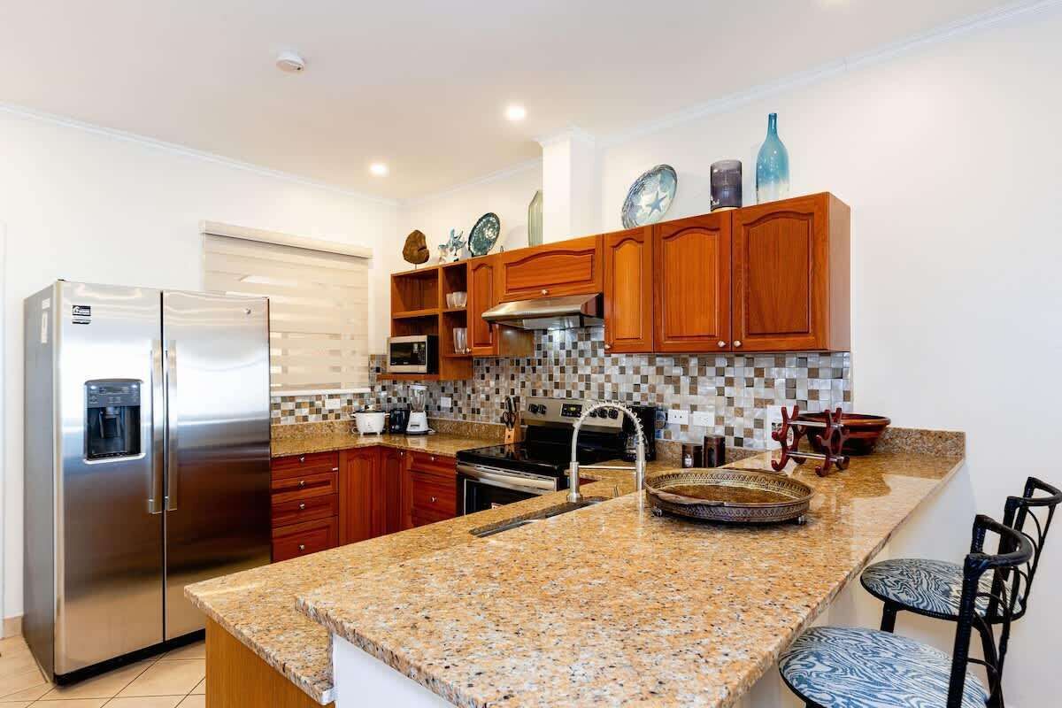 A modern kitchen with granite countertops, stainless steel appliances, wooden cabinets, and a tiled backsplash.