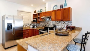 A modern kitchen with granite countertops, stainless steel appliances, wooden cabinets, and a tiled backsplash.