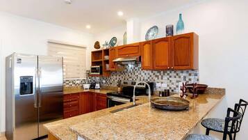 A modern kitchen with granite countertops, stainless steel appliances, wooden cabinets, and a tiled backsplash.