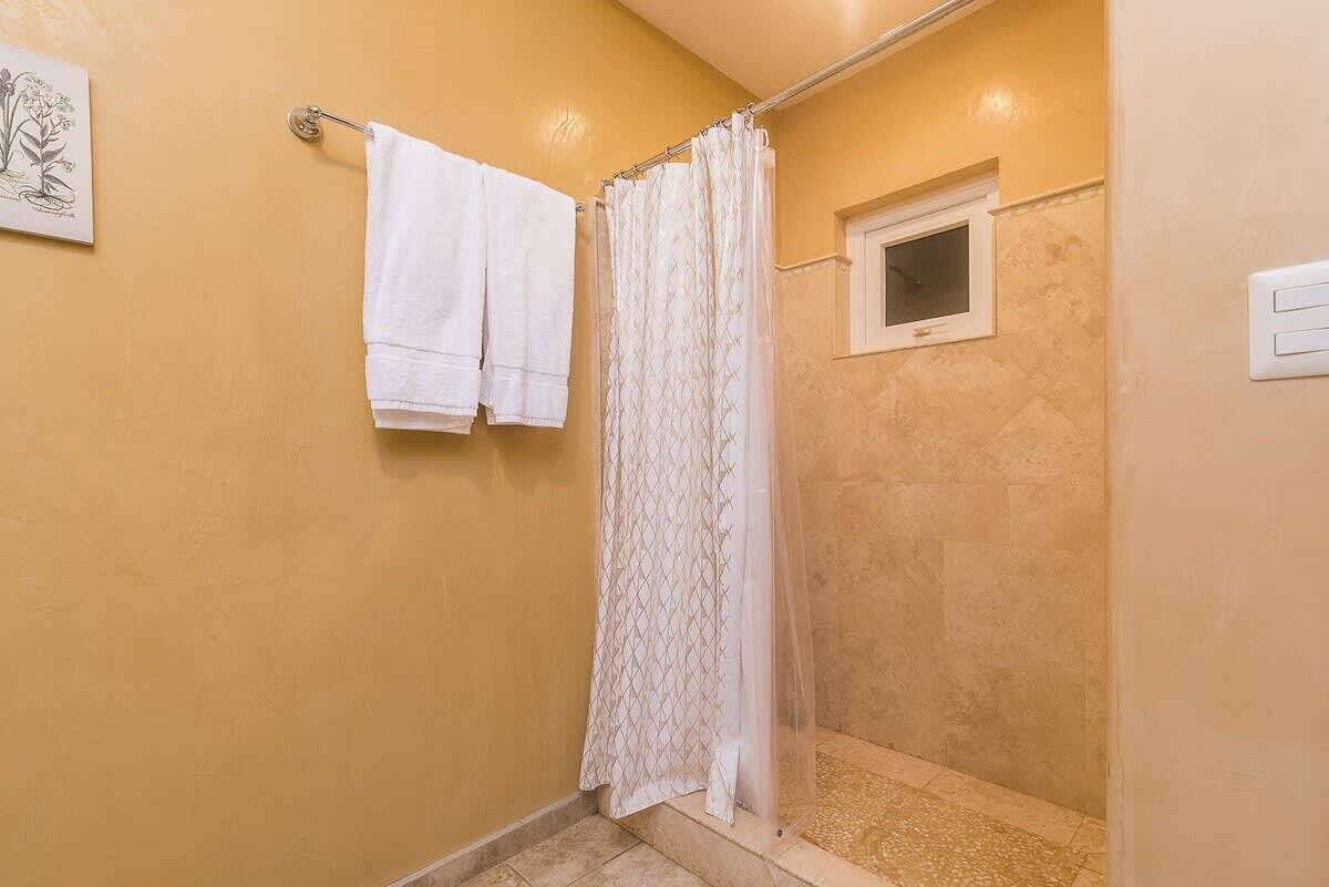 A small, enclosed shower area with a shower curtain, a window, and two white towels hanging on a metal rod.
