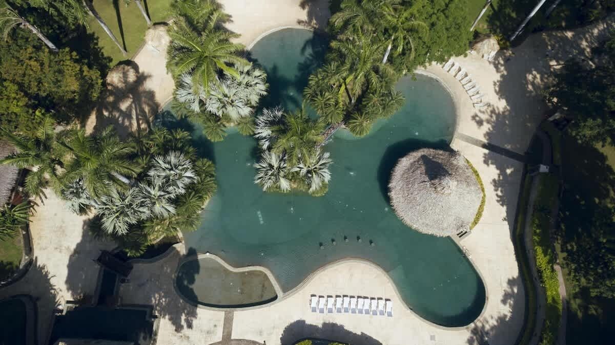 Luchtbeeld van een aangelegde tuin met een vijver in het midden, omringd door palmbomen en een rond zitgedeelte.