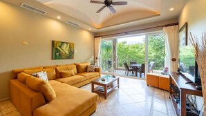 A living room with a sofa, coffee table, and a TV stand. There is a ceiling fan and a painting on the wall. - Matapalo 302- 2 Bedroom Condo at Tamarindo (Tamarindo)
