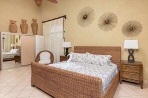 A bedroom with a wicker bed, a nightstand with a lamp, and decorative wall art.