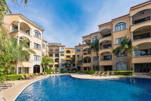 A hotel with a swimming pool surrounded by palm trees and sun loungers.