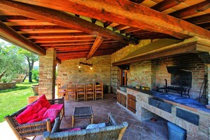Une terrasse extérieure dotée d’une cheminée en pierre, de meubles en osier et offrant une vue sur le jardin.