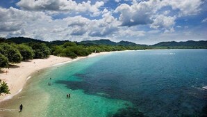 A beach with clear turquoise waters, a sandy shore, and a forested hillside.