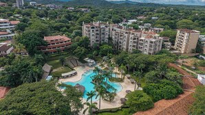 An aerial view of a resort with multiple buildings, a swimming pool, and lush greenery. - Matapalo 102- Poolside Condo at the Diria Resort- (Tamarindo)