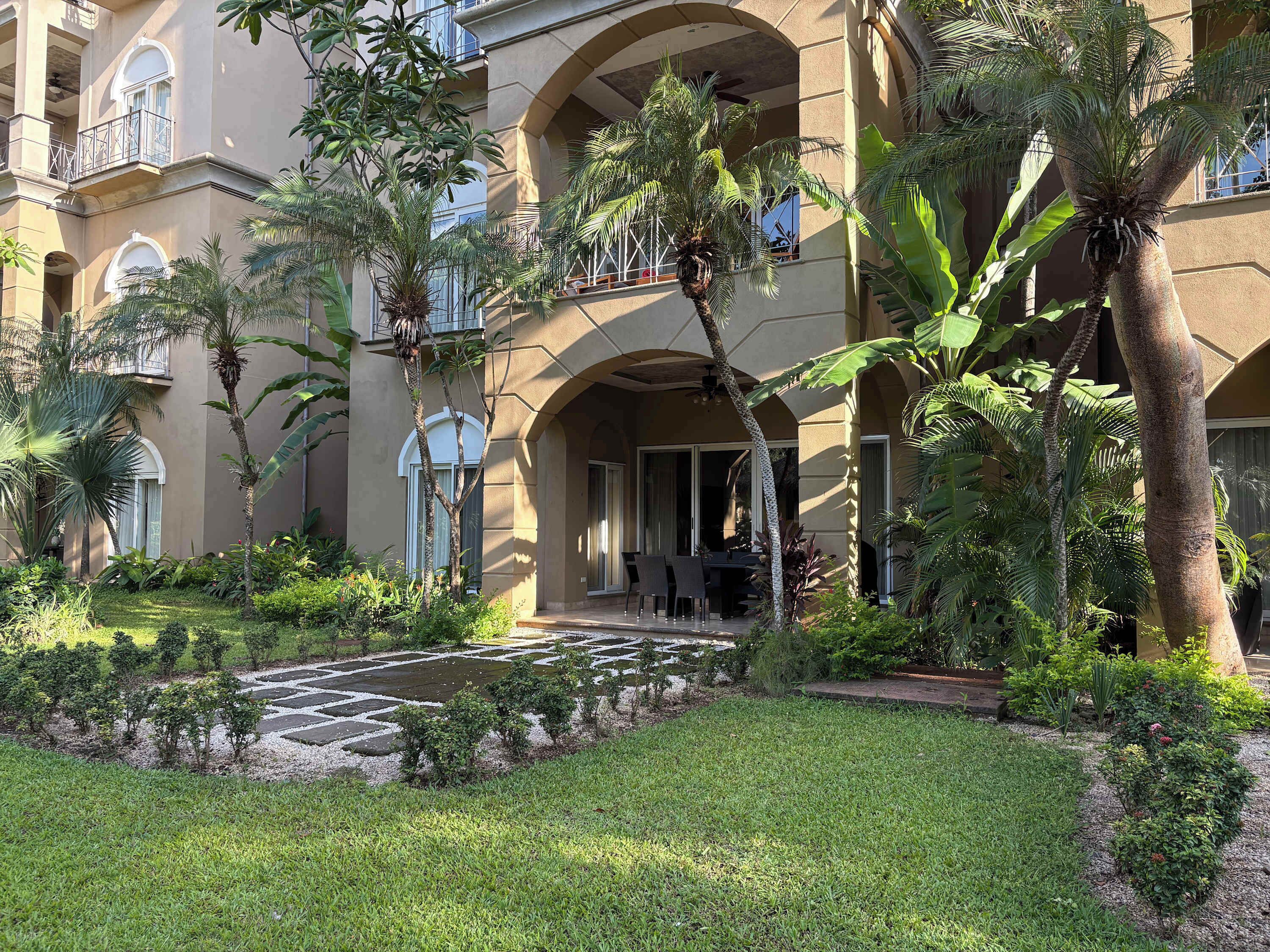 Pátio de hotel com piscina, palmeiras e área de estar coberta.