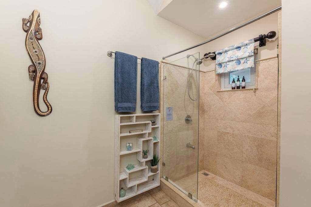 Et bruseområde med glasdør, to håndklæder hængende på en bøjle, og en hylde med toiletartikler.