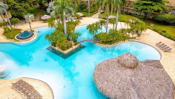 A resort pool area with a central water feature, lounge chairs, and palm trees. - Matapalo 102- Poolside Condo at the Diria Resort- (Tamarindo)