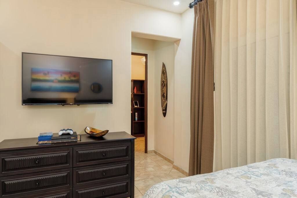 A bedroom with a bed, a dresser, a television, and a door leading to another room.