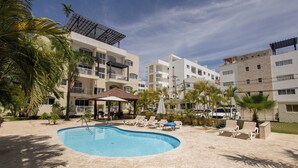 Une piscine entourée de chaises longues et de palmiers, avec des immeubles à plusieurs étages en arrière-plan.