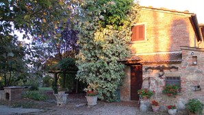 Un edificio rustico in pietra con una porta in legno, circondato da piante in vaso e un vialetto ghiaioso.