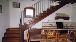Una scala in legno conduce a una sala da pranzo con tavolo e sedie, una cucina con un fornello e un portaposate a sospensione.