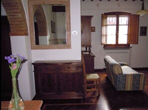 A traditional room with a wooden cabinet, a mirror, a patterned sofa, and a window with wooden shutters.