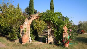 Un arco in pietra rustica con un cartello, circondato da vegetazione rigogliosa e piante in vaso.