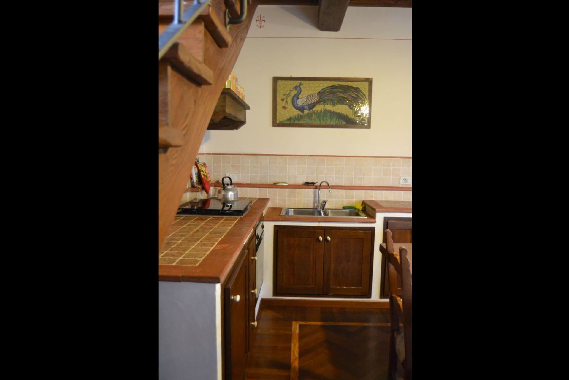 A kitchen with wooden cabinets, a sink, and a decorative peacock painting on the wall.