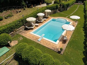 A rectangular swimming pool with a stone border, surrounded by grass and hedges.