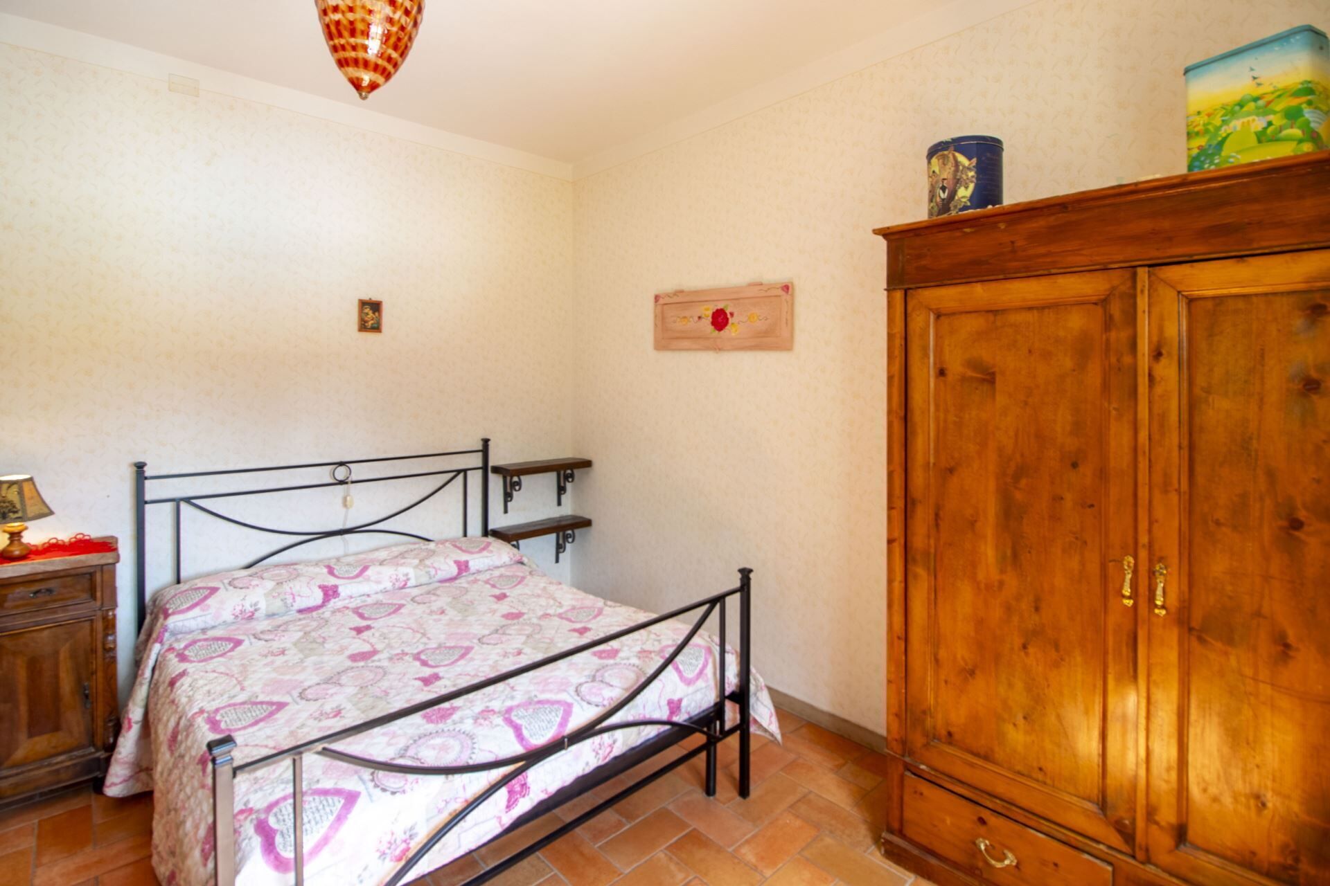 A bedroom with a bed, wooden wardrobe, and a small cabinet.