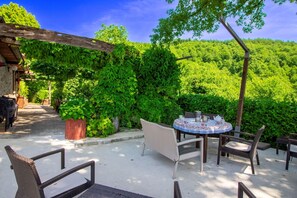 An outdoor patio with a table and chairs, surrounded by lush greenery and a clear blue sky.