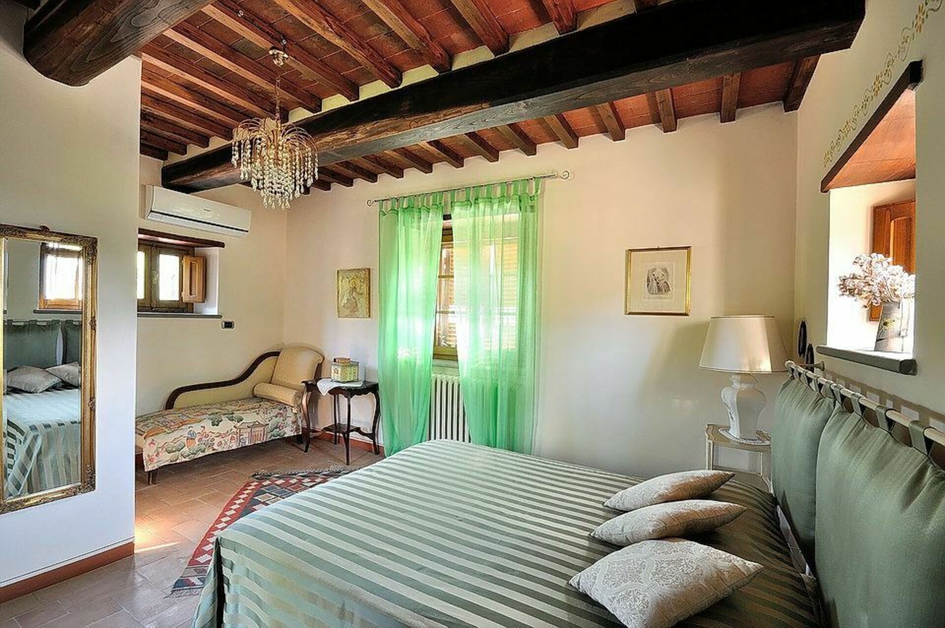 Un dormitorio con cama, una silla, una mesa y una ventana con cortinas verdes.
