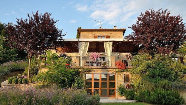A two-story house with a balcony, surrounded by lush gardens and trees.