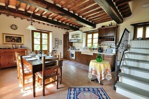 Una cucina rustica con travi in legno, un'area pranzo con tavolo apparecchiato per quattro persone e una scala.