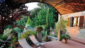 A patio with two chairs, a stone wall, and a wooden pergola.